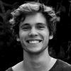 Technical SEO Company 3 A black and white portrait of a young man with wavy hair, smiling broadly and looking directly at the camera against a dark, blurry natural background.